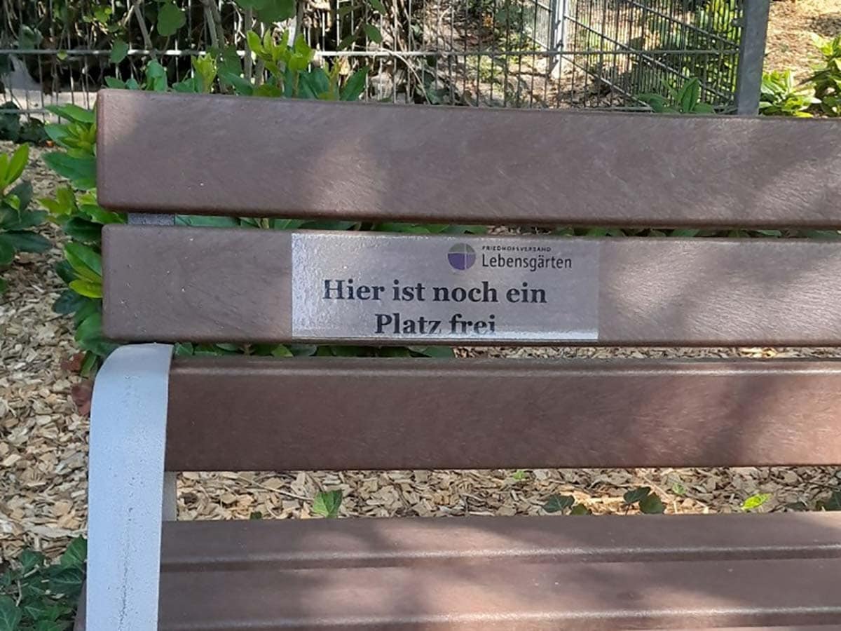 gesellige-bank-web Eine Parkbank mit einem Schild an der Rückenlehnen mit der Aufschrift "Hier ist noch Platz frei"